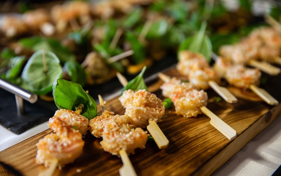 Crevettes frites croustillantes au sésame en brochettes, présentées sur une planche en bois rustique avec basilic frais.