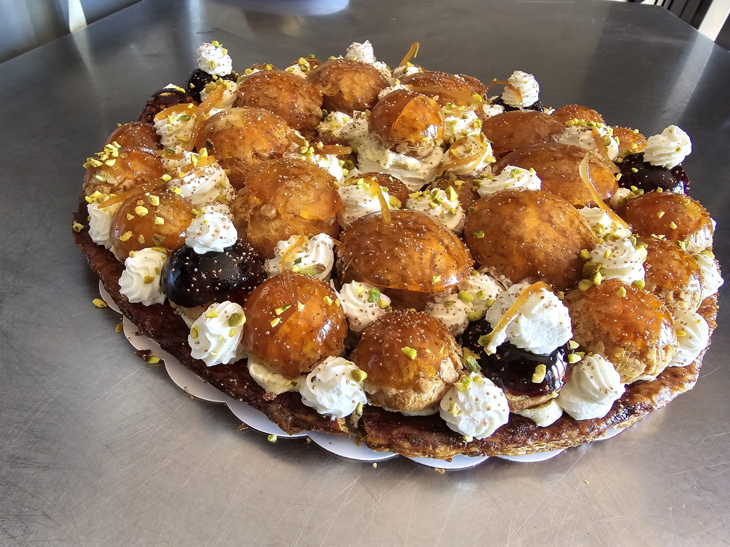 Gâteau Saint-Honoré gourmand aux choux caramélisés, crème chantilly et pistaches sur pâte feuilletée croustillante.