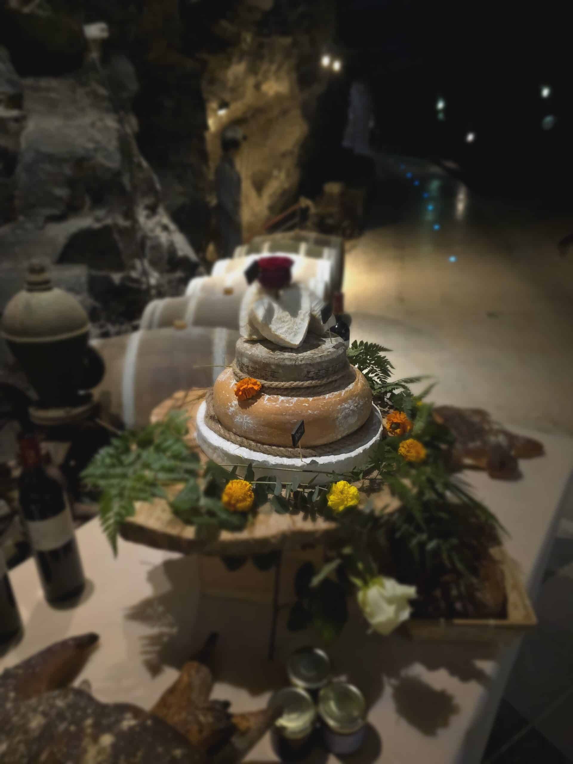 Pièce montée de fromages et fleurs sur bois dans une cave à vin avec tonneaux de chêne en arrière-plan.