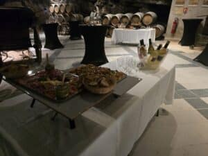 Buffet de charcuterie et vin blanc dans une cave voûtée avec fûts de chêne pour une réception élégante.