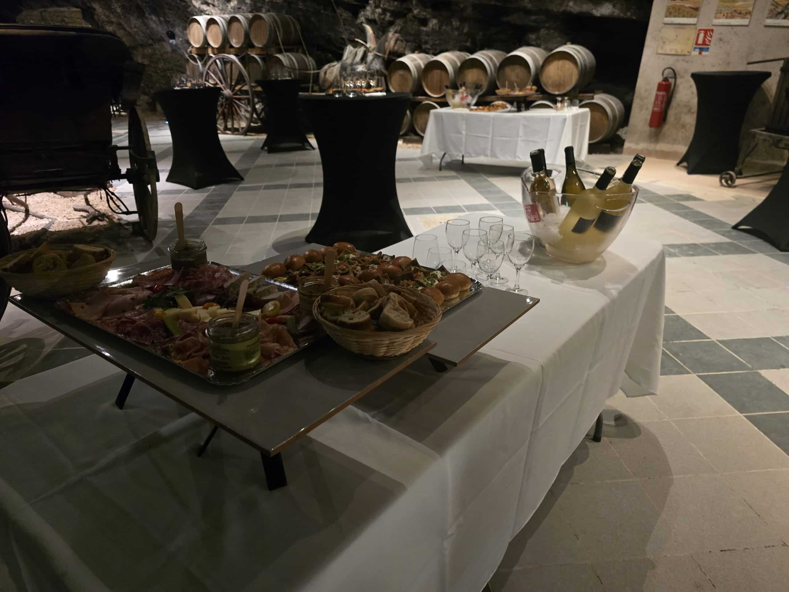 Buffet de charcuterie et vin blanc dans une cave voûtée avec fûts de chêne pour une réception élégante.