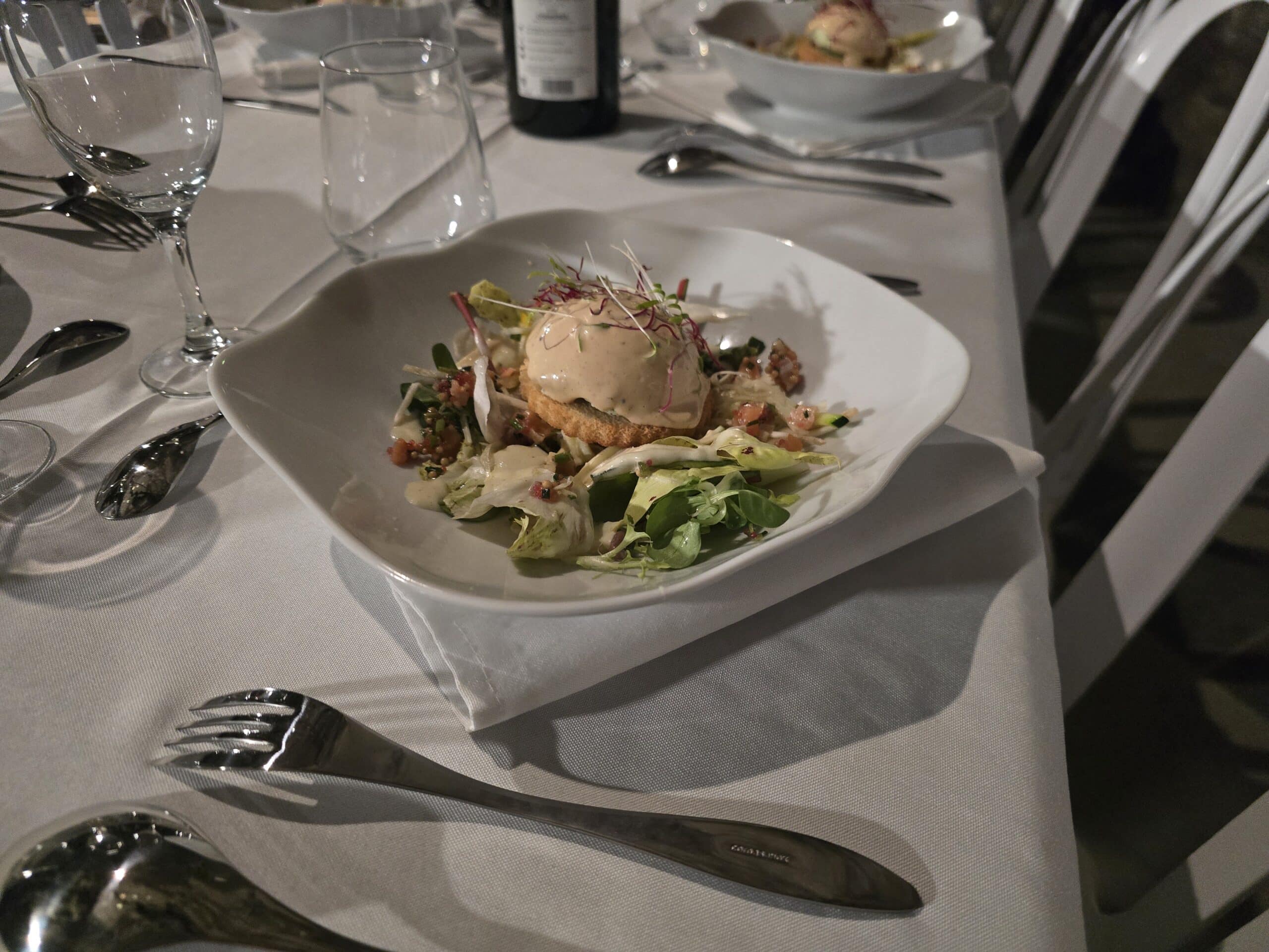 Entrée Gastronomique : Salade Raffinée et Mousse Onctueuse Entrée gastronomique avec salade, mousse onctueuse et jeunes pousses servie sur une nappe blanche élégante.